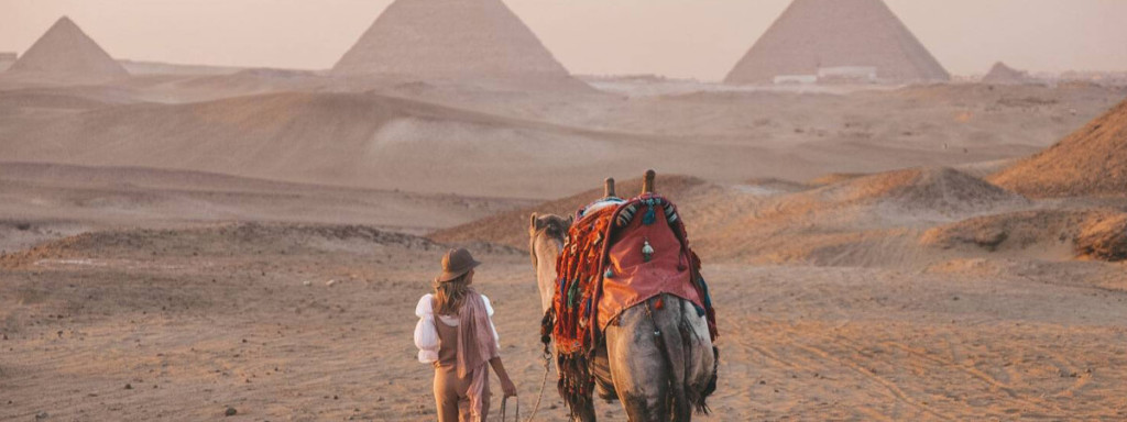 A picture of a tourist riding solo a camel in front of the Pyramids of Giza